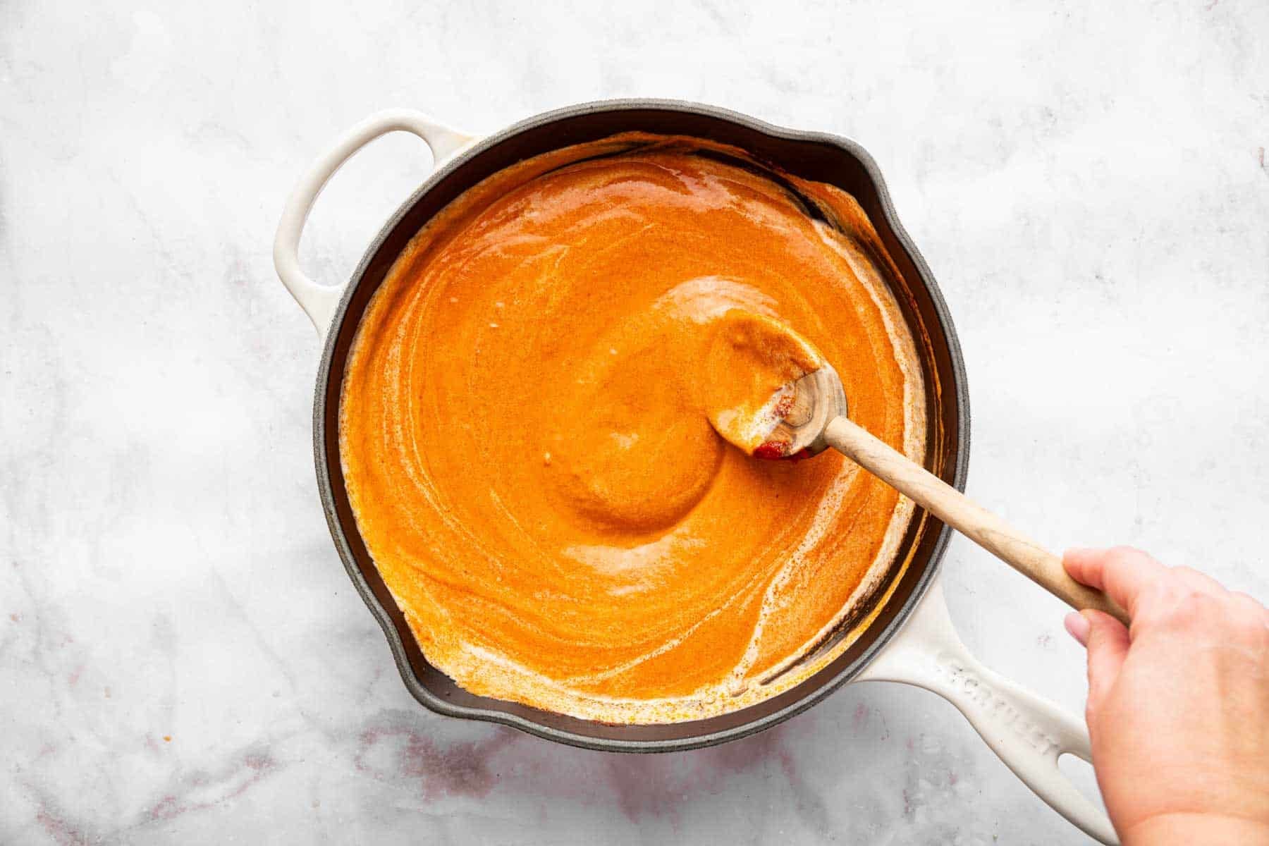 Orange sauce being stirred in a pan with a wooden spoon.