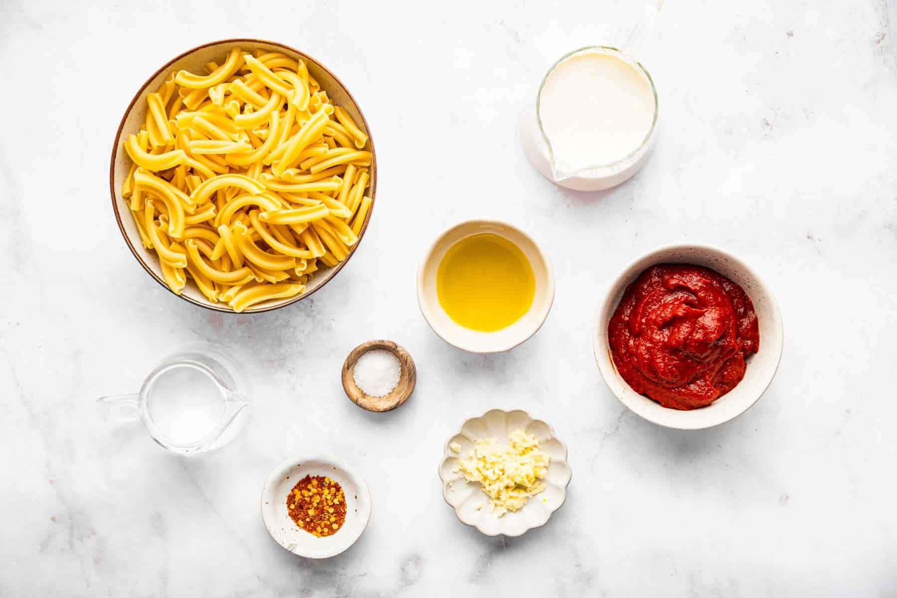 Bowl of raw pasta, tomato paste, spices and herbs on marble counter.
